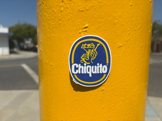 Yellow pole with a Chiquito logo sticker on a blurred outdoor background